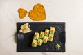 Sushi roll with avocado slices, red caviar on black plate, hearts of spices on marble background Royalty Free Stock Photo