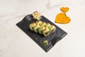 Sushi roll with avocado slices, red caviar on black plate, hearts of spices on marble background Royalty Free Stock Photo