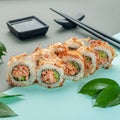 Sushi roll Bonito in tuna shavings. With fried salmon and cucumber. Decorated with greenery. In the background is a gravy boat and Royalty Free Stock Photo