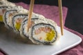 Sushi roll with chopsticks on a white plate close up. Pink napkin on a gray background Royalty Free Stock Photo