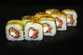 Sushi roll with cucumber, omelette, cheese and smoked salmon on a black background.