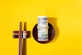 Sushi roll of dollars is tightened with a rubber band and sushi sticks on a yellow background Royalty Free Stock Photo