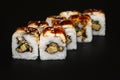 Sushi roll with eel and unagi sauce on black background.