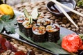 Sushi Roll - Maki Sushi with Smoked Eel, cucumber, avocado and sesame on black stone on bamboo mat decorated with flowers. Royalty Free Stock Photo