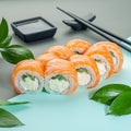 Sushi roll Philadelphia with salmon, cream cheese and cucumber. Decorated with greens. In the background is a gravy boat and