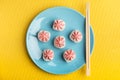 Sushi roll of rice with pink Lava sauce on a blue plate with chopsticks, on a yellow background