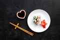 Sushi roll with salmon and avocado on plate with soy sauce, chopstick, wasabi on black background top view