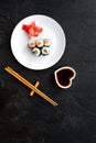 Sushi roll with salmon and avocado on plate with soy sauce, chopstick, wasabi on black background top view copyspace