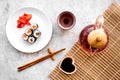 Sushi roll with salmon and avocado on plate with soy sauce, chopstick, wasabi near tea pot on grey stone background top Royalty Free Stock Photo