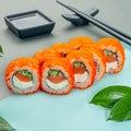 Sushi roll with salmon, butter cream and cucumber. Sprinkled with masago caviar. Decorated with greenery. In the background is a Royalty Free Stock Photo