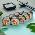 Sushi roll with salmon cheese and cucumber. Decorated with greenery. In the background is a gravy boat and chopsticks. Close-up