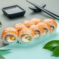 Sushi roll with salmon and eel, cream cheese and jalapeno. Decorated with greenery. In the background is a gravy boat and