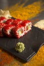 Sushi roll with salmon, red flying fish roe Tobiko with wasabi, ginger on black plate, Scattered spices on background Royalty Free Stock Photo