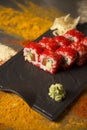 Sushi roll with salmon, red flying fish roe Tobiko with wasabi, ginger on black plate, Scattered spices on background Royalty Free Stock Photo