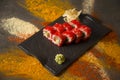 Sushi roll with salmon, red flying fish roe Tobiko with wasabi, ginger on black plate, Scattered spices on background Royalty Free Stock Photo