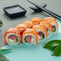 Sushi roll with salmon and tuna. Decorated with greenery. In the background is a gravy boat and chopsticks. Close-up