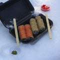 Sushi rolls in a black box in the snow. California with salmon in sesame and Philadelphia with salmon, cucumber and cheese. Royalty Free Stock Photo