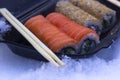 Sushi rolls in a black box in the snow close-up. California with salmon in sesame and Philadelphia with salmon, cucumber and