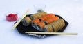 Sushi rolls in a black plate in the snow close-up. California with salmon in sesame and Philadelphia with salmon, cucumber and