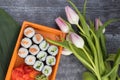 Sushi Rolls with cucumber and red fish in an orange container on a dark background next to flowers, pink tulips, top Royalty Free Stock Photo