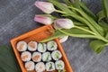 Sushi Rolls with cucumber and red fish in an orange container on a dark background next to flowers, pink tulips, top Royalty Free Stock Photo