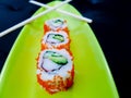 Sushi rolls on a green plate with chopsticks - avocado and crab maki  with tobiko caviar on dark background Royalty Free Stock Photo