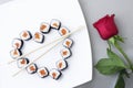 Sushi rolls laid out in the shape of a heart on a white plate. Red rose on a gray background. Creative greetings. The concept of Royalty Free Stock Photo