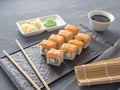 Sushi rolls philadelphia on a black textured plate stand on a gray background. wasabi ginger and sauce chopsticks. Rolls with Royalty Free Stock Photo