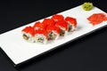 Sushi rolls set with red caviar and cream cheese served on a white plate over black background. Royalty Free Stock Photo