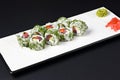 Sushi rolls with tuna, cucumber and cream-cheese in chopped dill. Served on a white plate over black background. Royalty Free Stock Photo