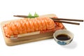 Sushi, salmon, and chopsticks are put on a wooden chopping board There is a sauce cup on the side. Royalty Free Stock Photo