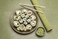 Sushi and sliced cucumbers on ceramic plate. Green bamboo mat for making sushi, chopsticks and wasabi in bowl Royalty Free Stock Photo