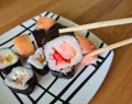 Sushi sticks in hands and set of rolls on plate. Delicious sushi with sliced rice and fresh vegetables Royalty Free Stock Photo