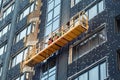 Suspended construction craddle near wall of hightower residentaial building with insulation and ventilated facade on