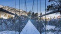 A suspended pedestrian bridge with mesh railings leads over a frozen river to a rocky island. Royalty Free Stock Photo