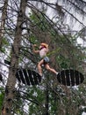 In a hanging rope park, a teenage boy climbs between trees on a hanging obstacle