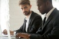 Suspicious Caucasian worker looking madly at busy black colleagu Royalty Free Stock Photo