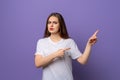 Suspicious teen girl pointing fingers aside, squinting and looking with doubtful face expression, standing over purple background Royalty Free Stock Photo