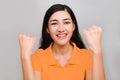 Sussess woman,young beautiful asian female in orange t-shirt pick up her hands smiling ,win isolated on gray background