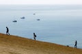 Silhouette of people climbing the white chalk cliffs in the Seven Sisters Country Park. Boats in the background