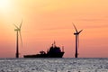 Sustainable resources. Wind farm with ship silhouette at tropical sunrise or sunset. Solar and wind energy and food supply Royalty Free Stock Photo