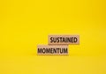 Sustained momentum symbol. Wooden blocks with words Sustained momentum. Beautiful yellow background. Business and Sustained