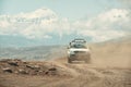 Suv car high in mountains drives along dusty mountain road against background of snowy mountains. Royalty Free Stock Photo