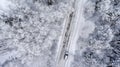 Suv driving in white snowy evergreen forest on slipery asphalt road. Aerial view from drone