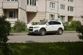 The SUV is parked. A white car stands on the street