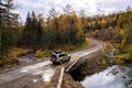 SUV on wooden bridge over small mountain river. Autumn forest Royalty Free Stock Photo
