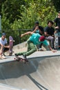 Young Adult Male Skateboarder Drops In As Other Skateboarders Watch