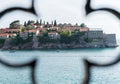 Sveneti Stefan in Budva Montenegro through a metal fence. Adriatic sea with boats and an old small town in a island. Stone luxury