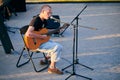 Young guy playing acoustic guitar and singing song in microphone, folk rock outdoor concert Royalty Free Stock Photo