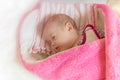 Swaddled adorable newborn girl is sleeping in bed